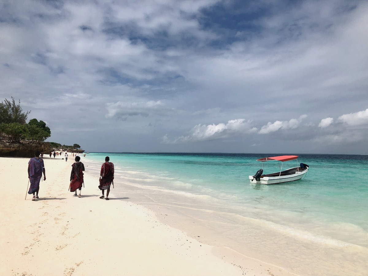 Three men in traditional attire walk on the beach in Zanzibar