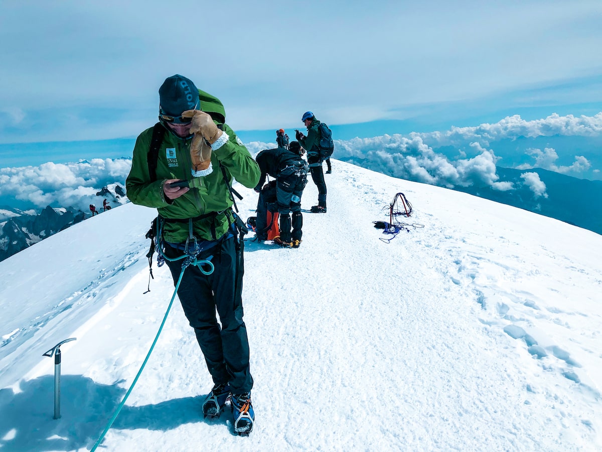 A mountain guide plays on his phone on the top of Mont Blanc's snowy summit.