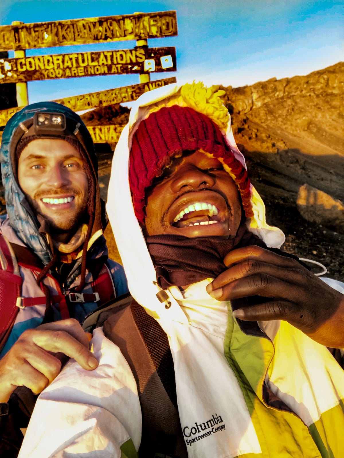 Two men smile with mountain gear on.
