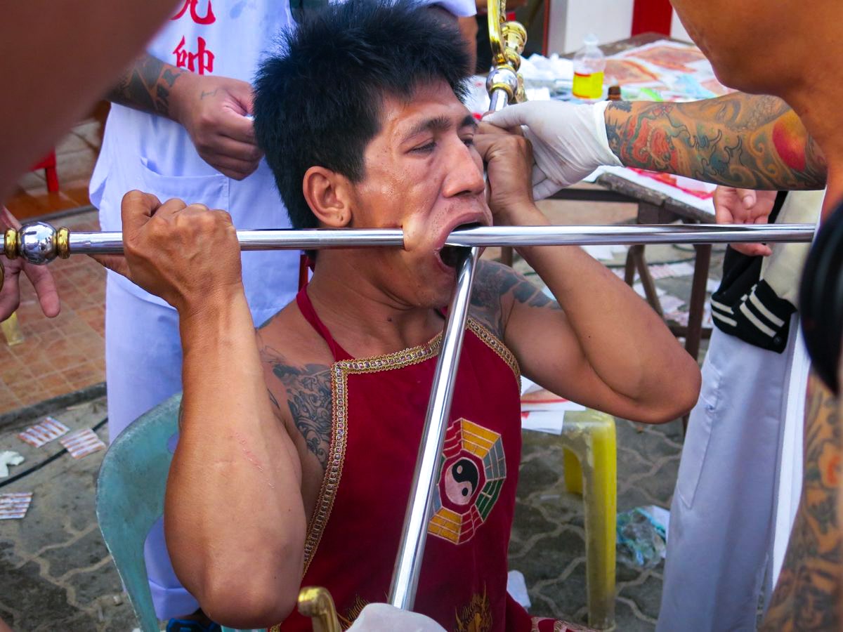 An Asian man with two large metal poles impaled through his face at the Phuket Thailand Festival