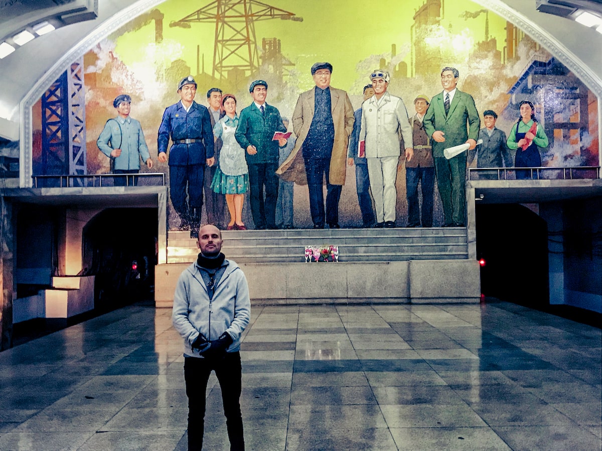 A male tourist stands in front of art depicting propaganda of the North Korean revolution in Pyongyang Metro Station