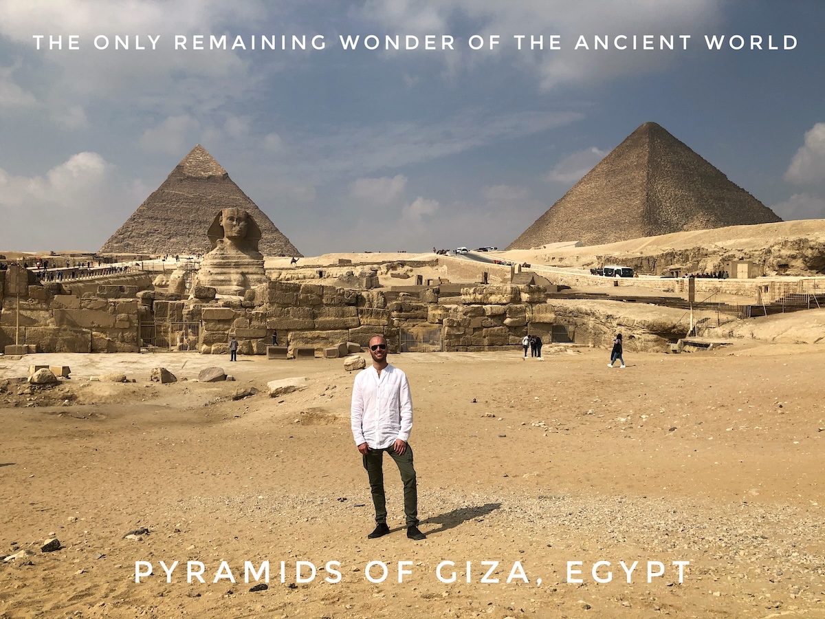 Man in white shirt and sunglasses poses in front of the Pyramids of Giza, Egypt.