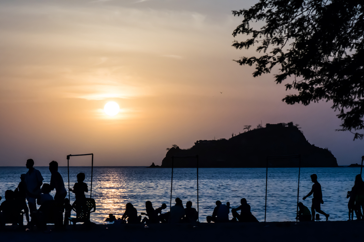 A silhouette of people walking and relaxing on a beach as the sun goes down in Santa Marta, Colombia.
