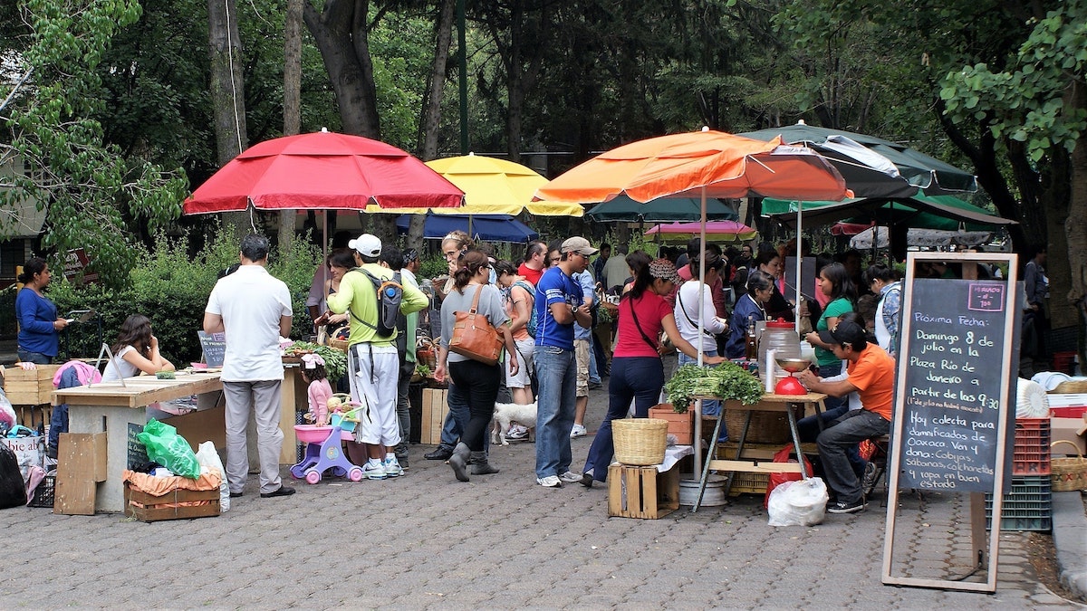 People gathering under colourful large umbrellas in a street market in Roma Norte in Mexico City.