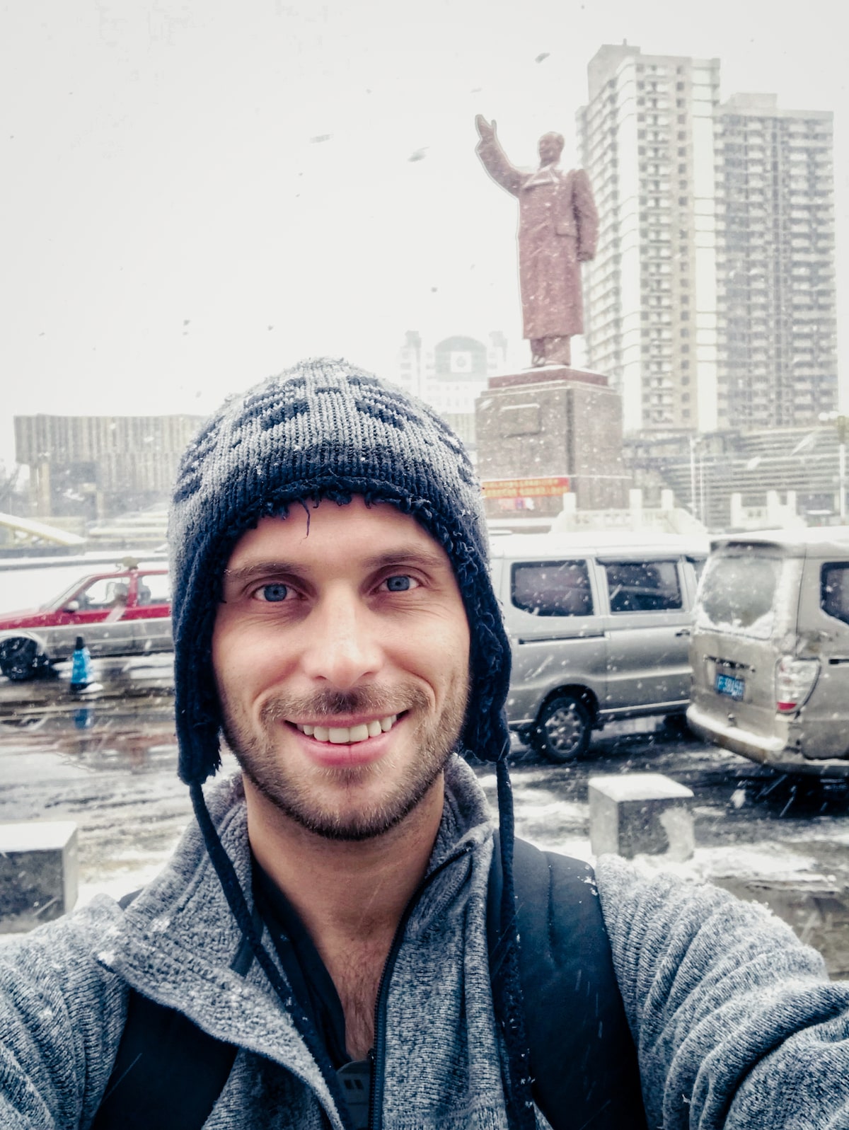 A male tourist in a winter hat poses in the snow in front of a large Chairman Mao statue in Dandong., China