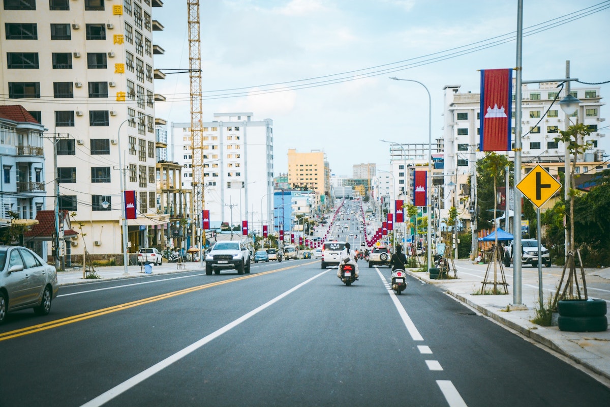 A busy highway with motorbikes and cars with Cambodian flags raised on the side of the road