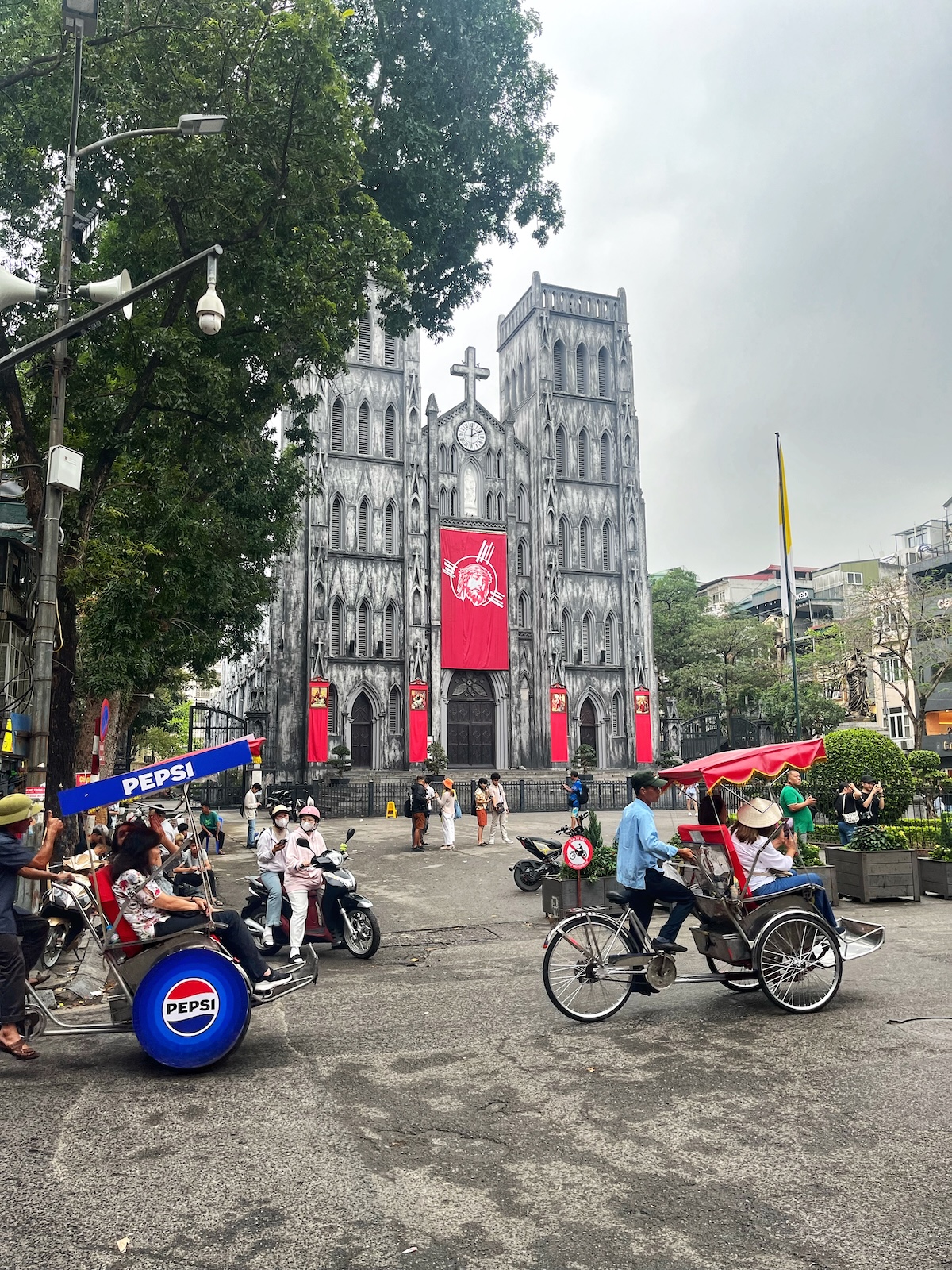 A grey gothic building with red decorations in front of busy traffic in central Hanoi, Vietnam
