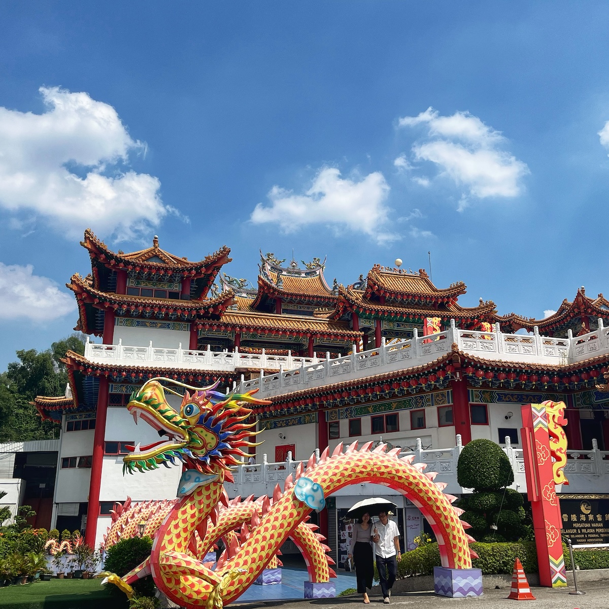 Colorful dragon sculpture and the ornate architecture of Thean Hou Temple in Kuala Lumpur, Malaysia, under a clear blue sky with a few clouds. Visitors are walking near the entrance, highlighting the temple's vibrant design and traditional Chinese elements.