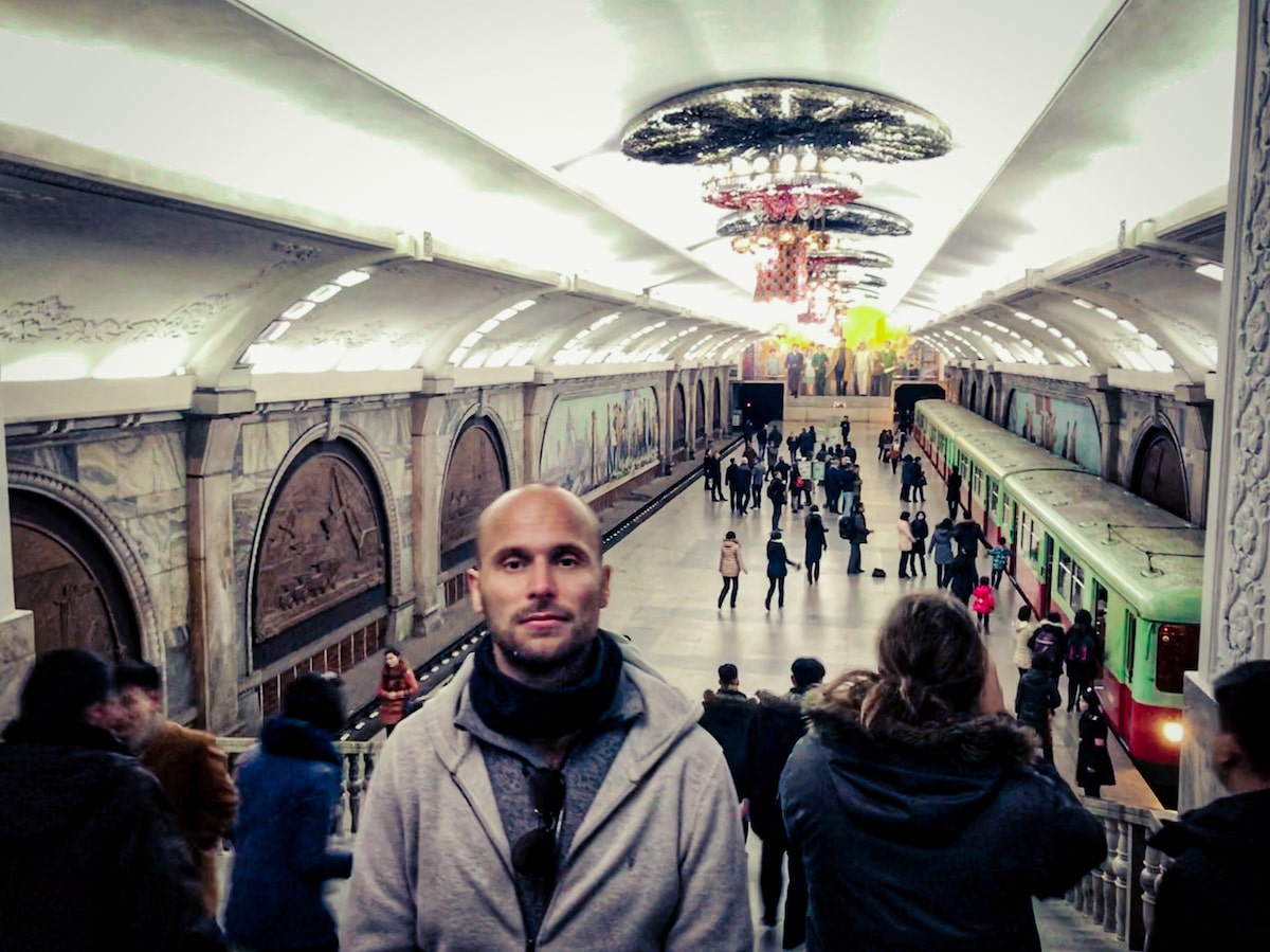 A male tourist poses in front of a rustic underground in Pyongyang Metro Station, North Korea