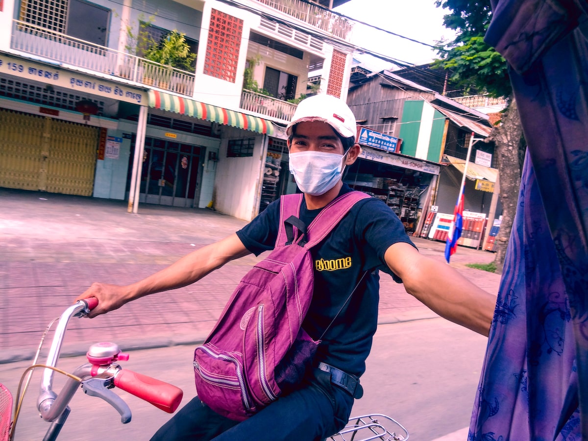 A man smiles in a pollution mask as he holds onto a tuk-tuk in Phnom Penh, Cambodia 