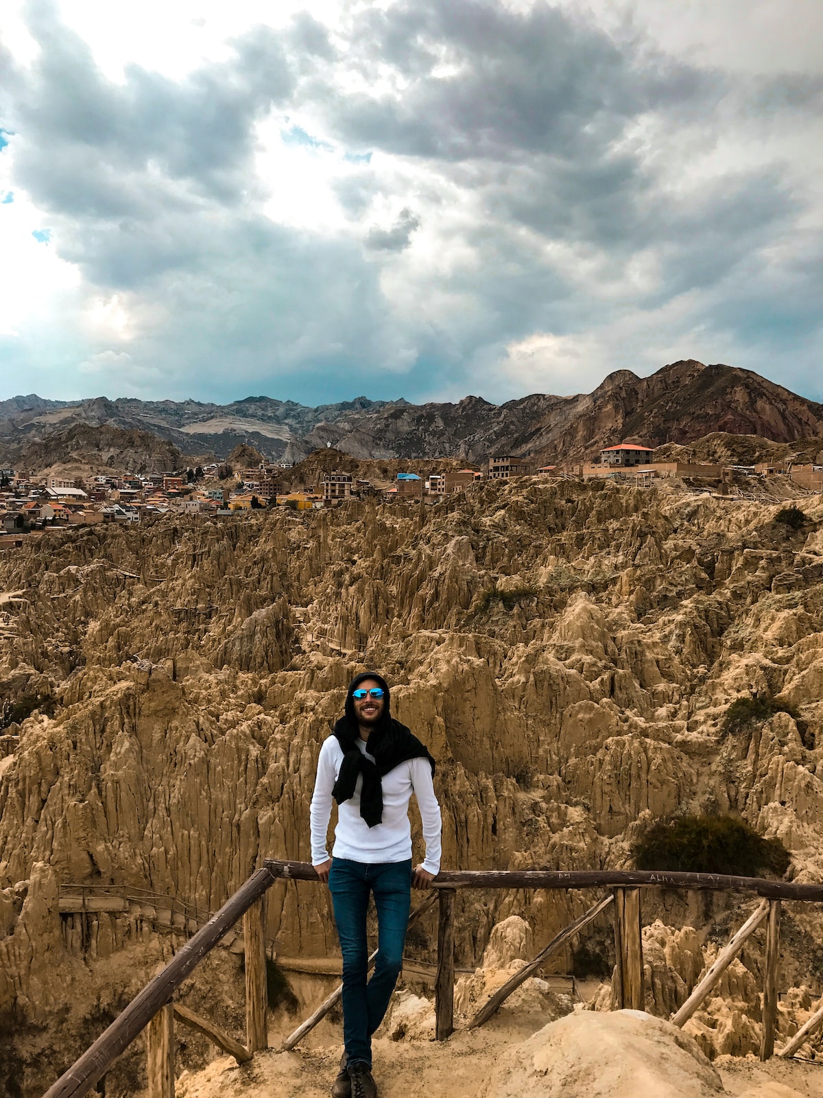 A man in sunglasses smiles in a white t-shirt in front of rock formations in La Paz, Bolivia.