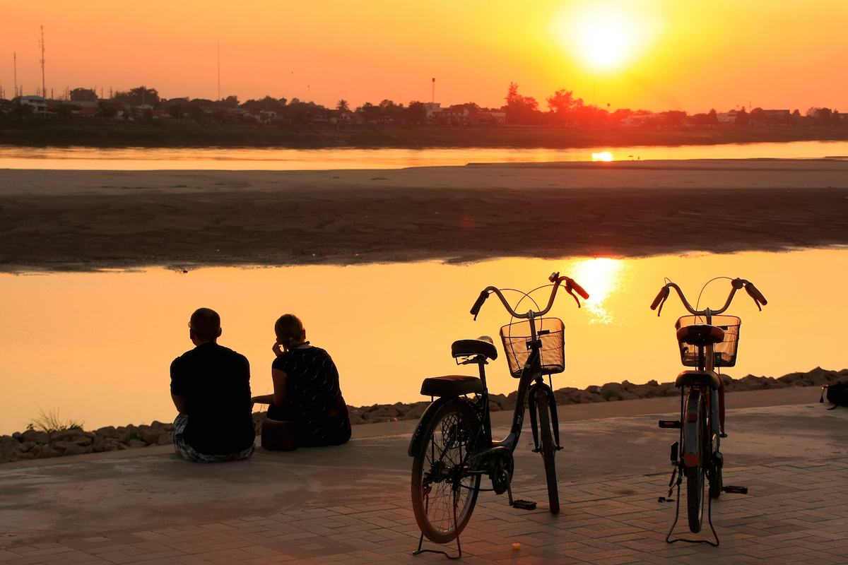 Silhouetted couple watching the sunset at Mekong river waterfront, Vientiane, Laos