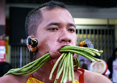 A man with long green vegetables pierced through his cheeks.