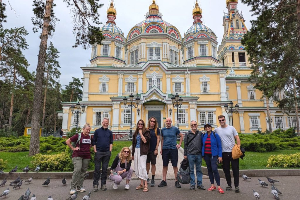 Travellers outside the yellow and multicoloured Ascension Cathedral in Almaty, pigeons on the path