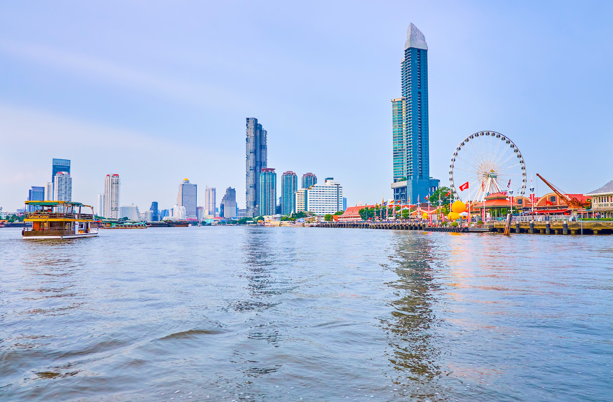 The view of the banks of a river with modern skyscrapers, residential houses and a large Ferris wheel. 