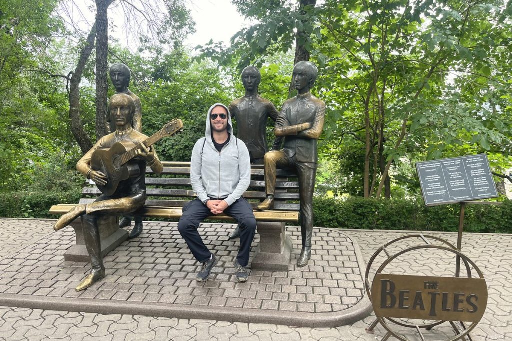 The Beatles bronze monument at Kok Tobe, Almaty, with a visitor sitting on the bench