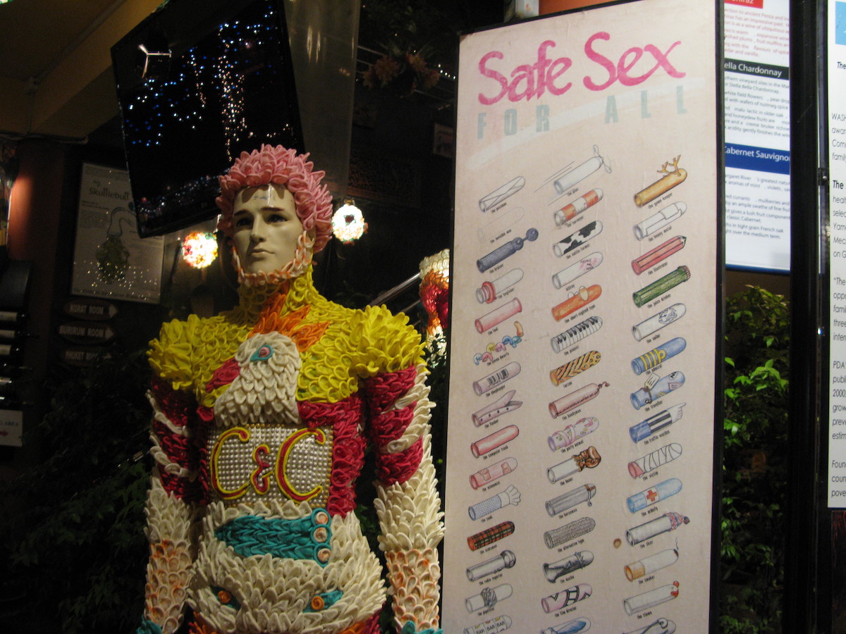 A mannequin covered in flowers stands next to a sign depicting different condoms.