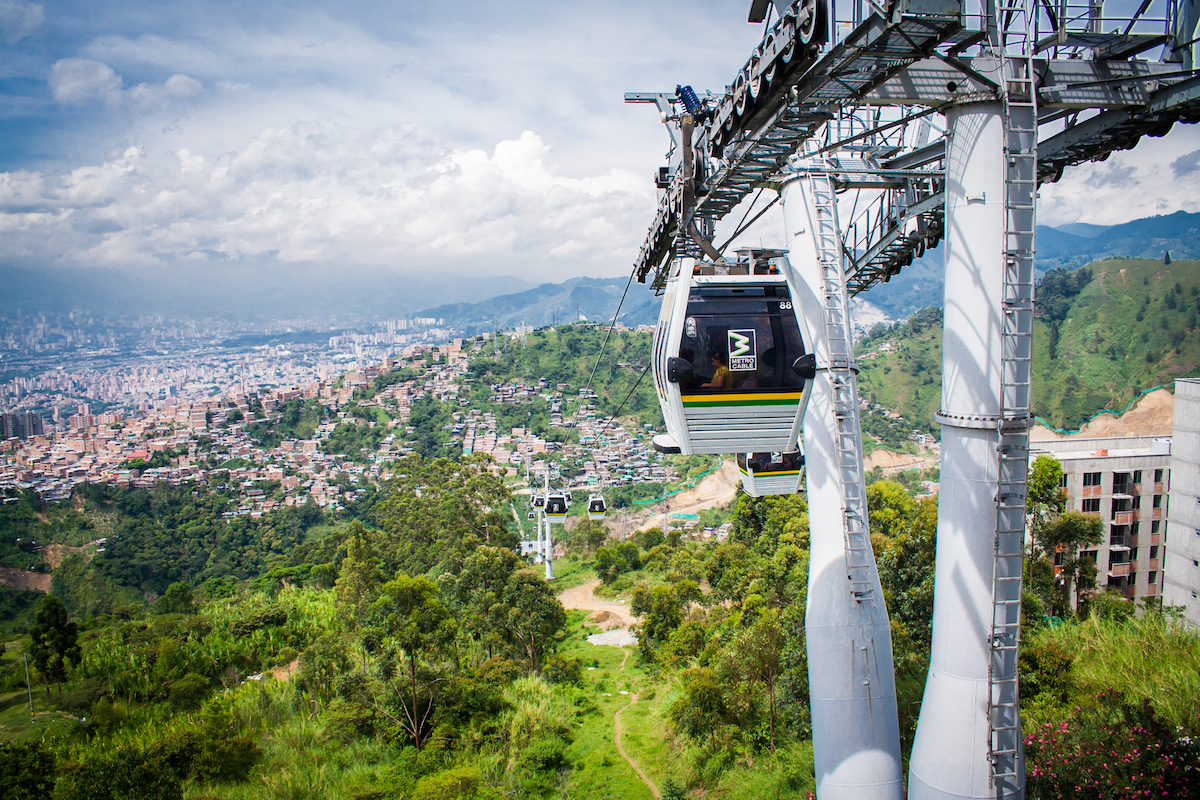 A cable car moves as it overlooks green trees, mountains and the city centre on a sunny day in Medellin. 