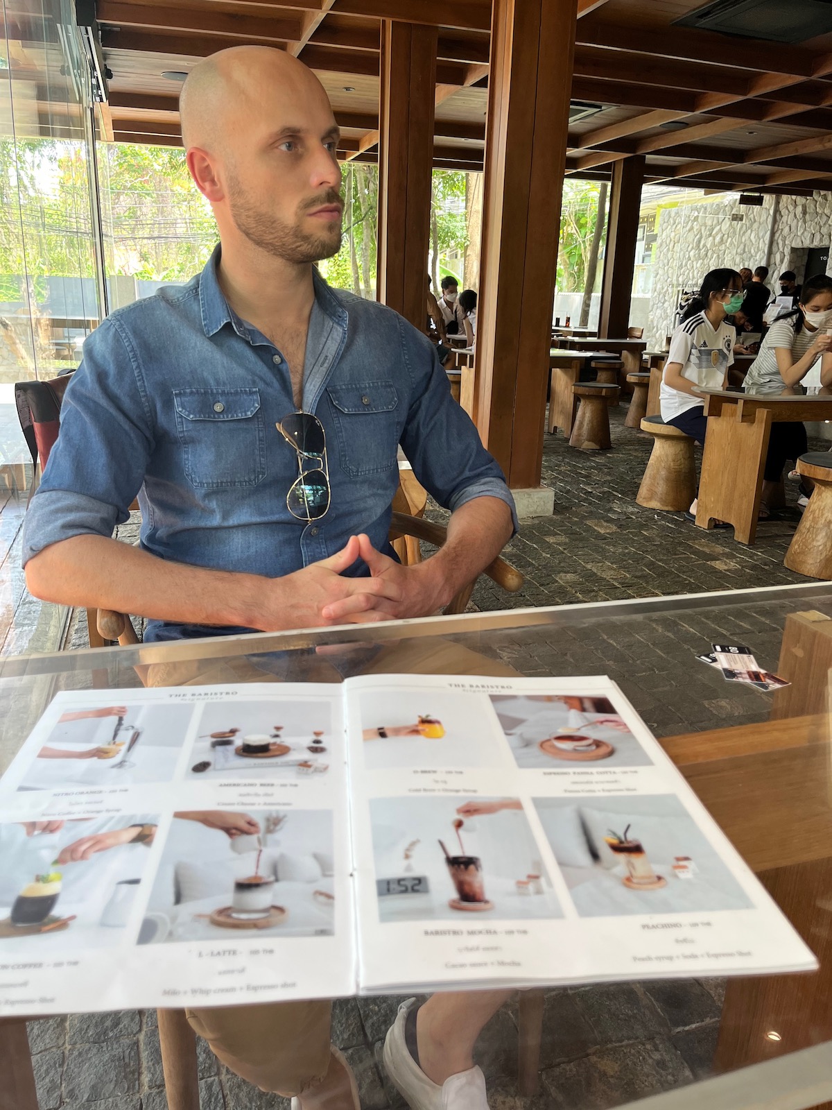 A man with a shaved head and beard looks to the side while waiting in a cafe in Chiang Mai