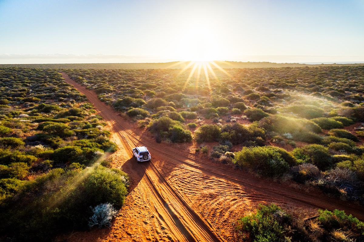 A campervan driving through the desert on a sunny day in Australia.