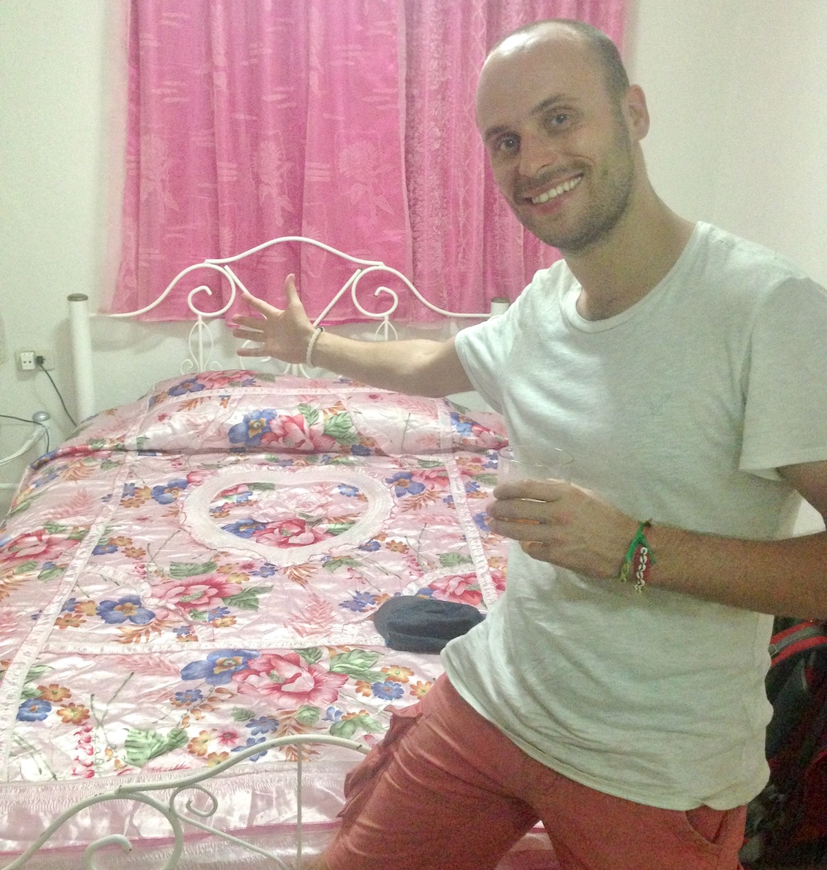 A man smiles goofily in a pink bedroom in a Casa Particular in Havana, Cuba