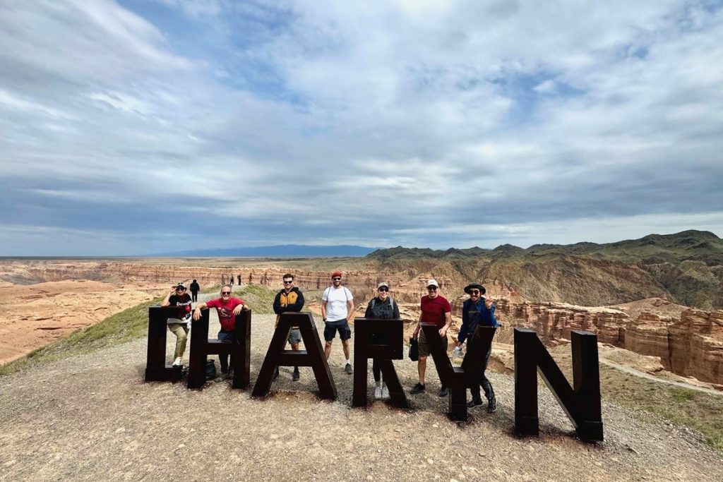 Tour group standing at the large Charyn letters sign above the canyon, Kazakhstan