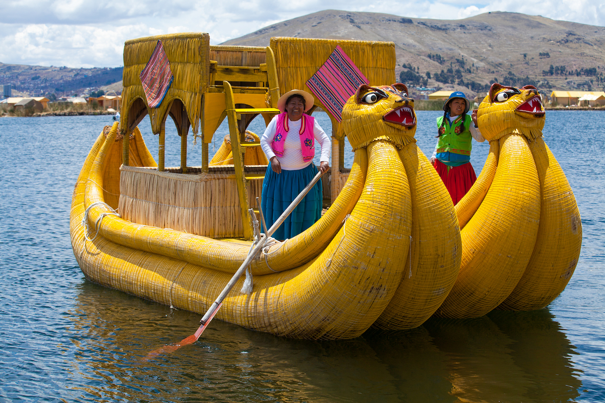 A women in traditional dress smiles on a local boat in Lake Titicaca