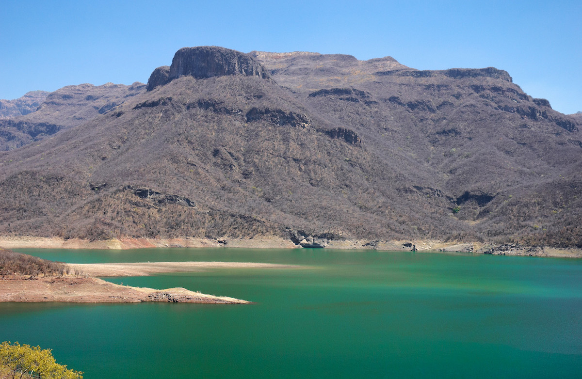 A copper-coloured mountain overlooks turquoise water.