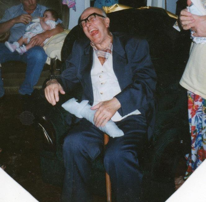 An old man laughs open-mouthed, surrounded by his family 
