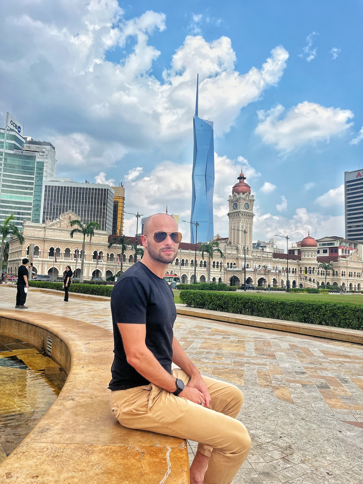 A male tourist in sunglasses poses in front of a striking government building and modern architecture in Kuala Lumpur, Malaysia 