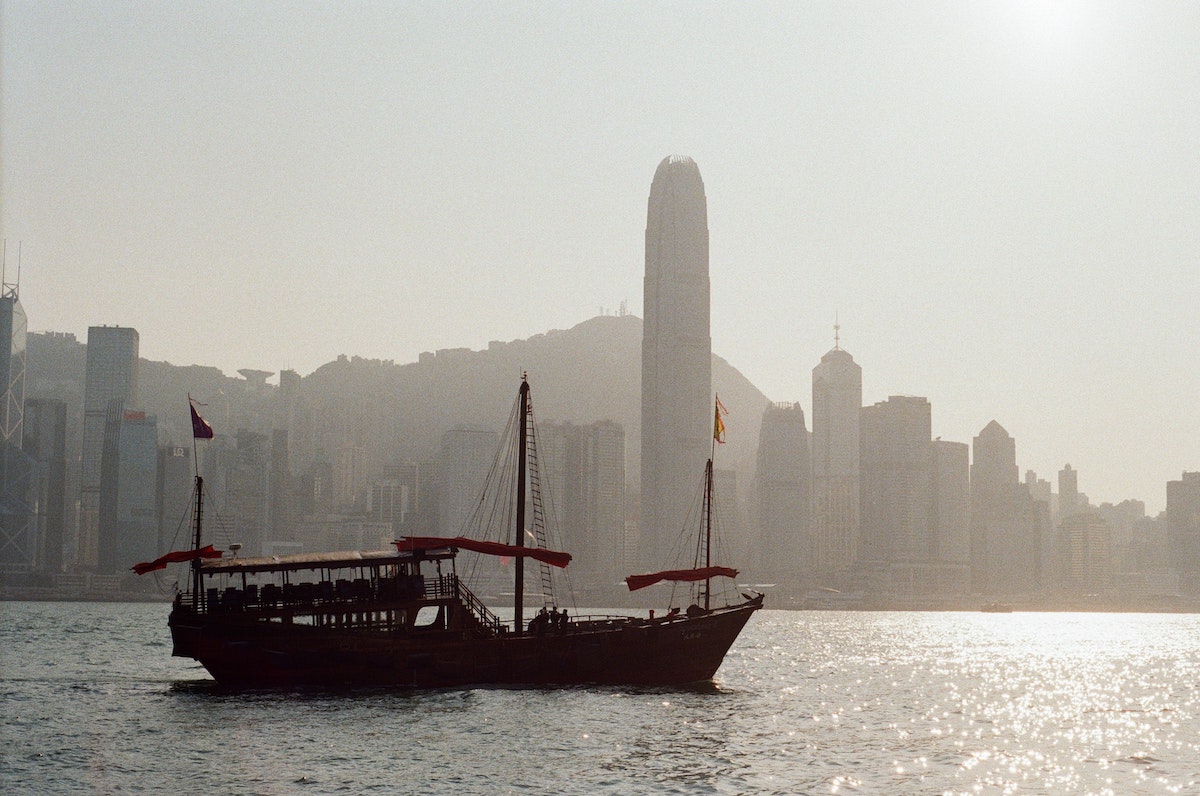 A large traditional ship sails across a harbour with skyscrapers in Hong Kong