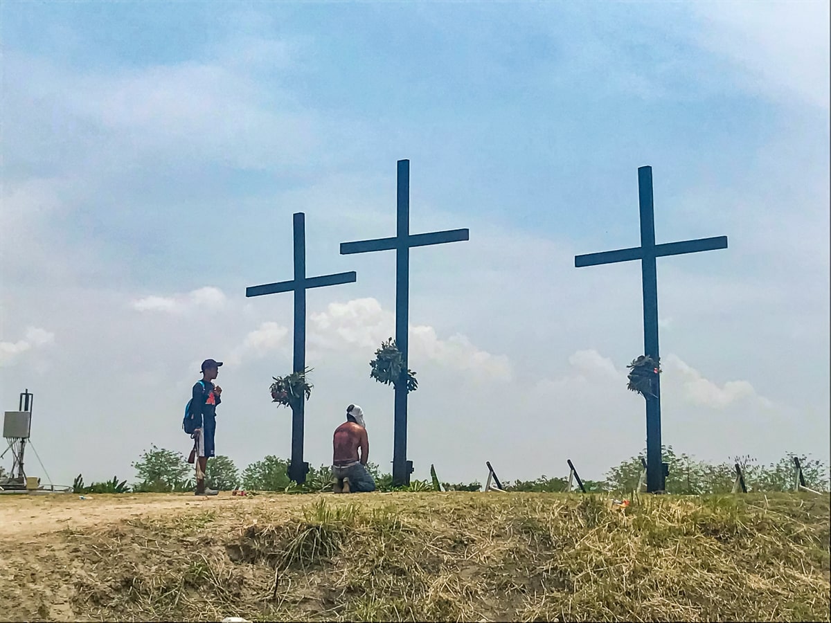A shirtless man kneels in front of three raised crucifixes in The Philippines 