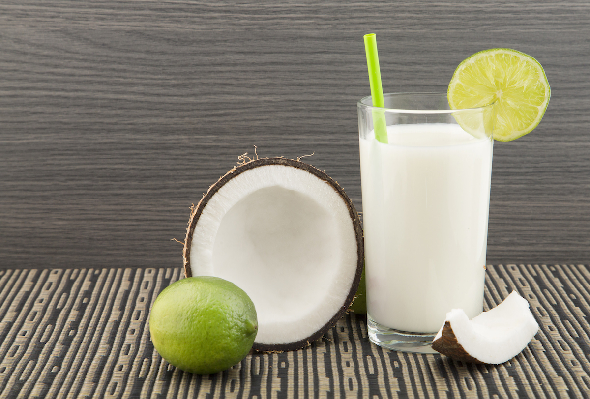 A white liquid in a glass with lime and coconut on the side.