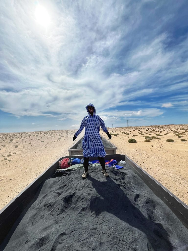 Man riding on top of the iron ore train in Mauritania poses s the train goes through the Sahara Desert