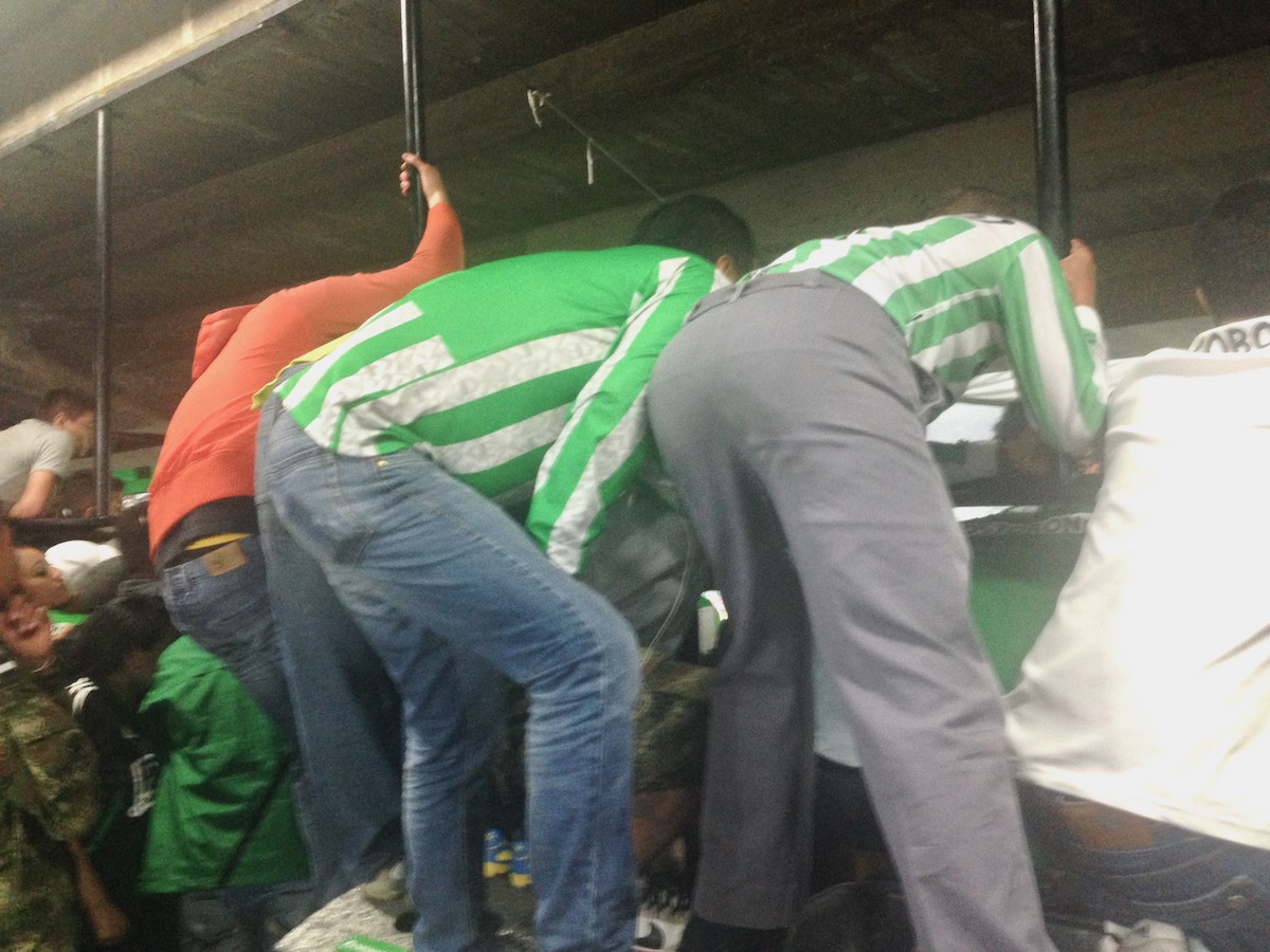 Football fans in green and white stripes climb over a barricade.