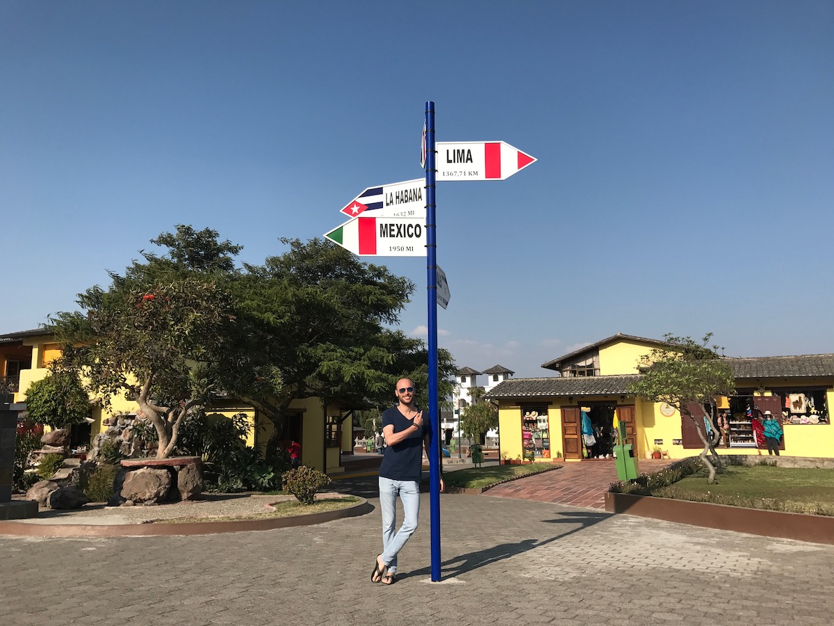 A man smiles under a signpost pointing to Peru, Cuba and Mexico in La Mitad del Mundo in Quito