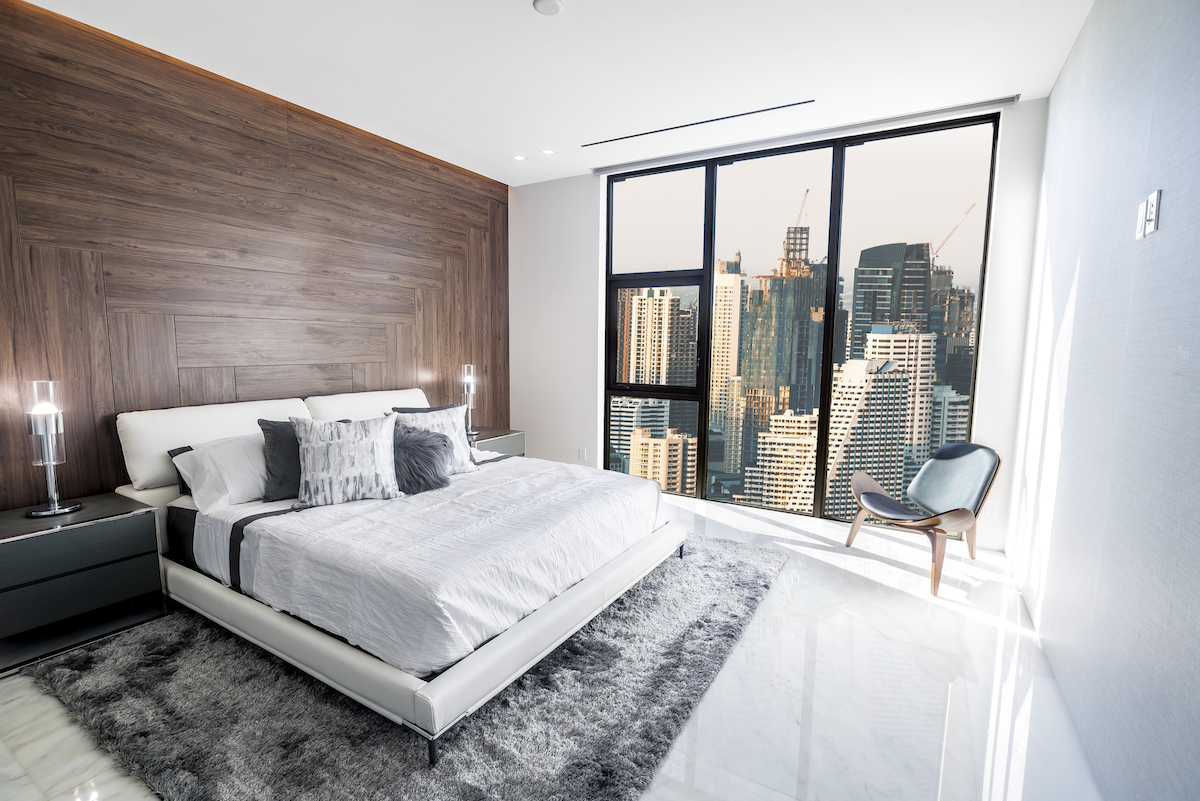 Modern and luxurious condo bedroom with white ceiling and wood accents with views of Bangkok skyline