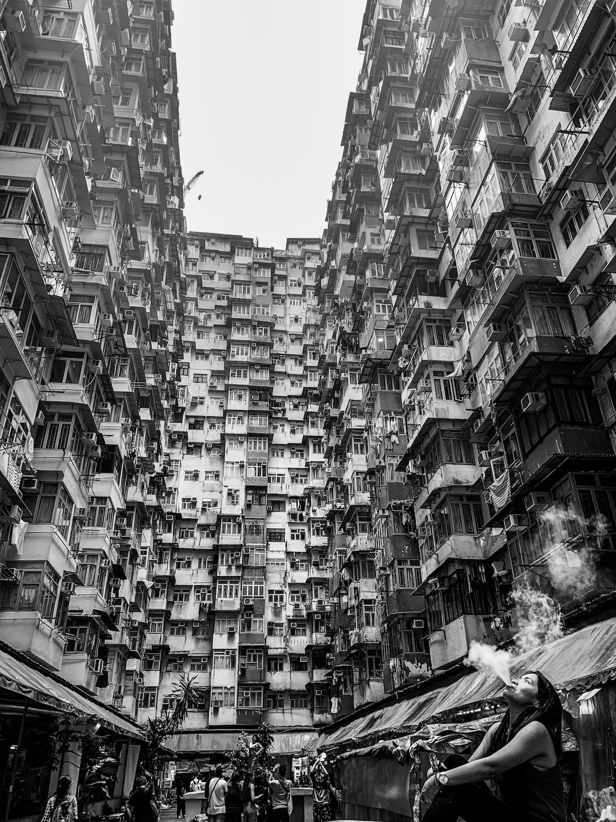 A lady blows smoke into the air below a busy set of flats, knowns as The Monster Building in Hong Kong.