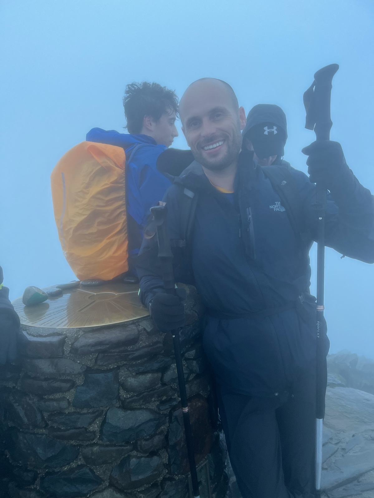 A hiker smiles on top of Mount Snowdon's summit