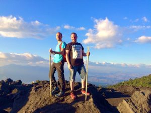 Two men stand back to back with wooden walking sticks after summiting Pacaya Volcano at sunset.