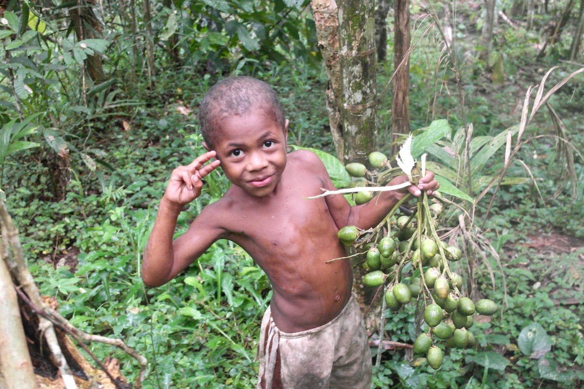 A boy smiles as he collects fruit in the jungles of Papua New Guinea