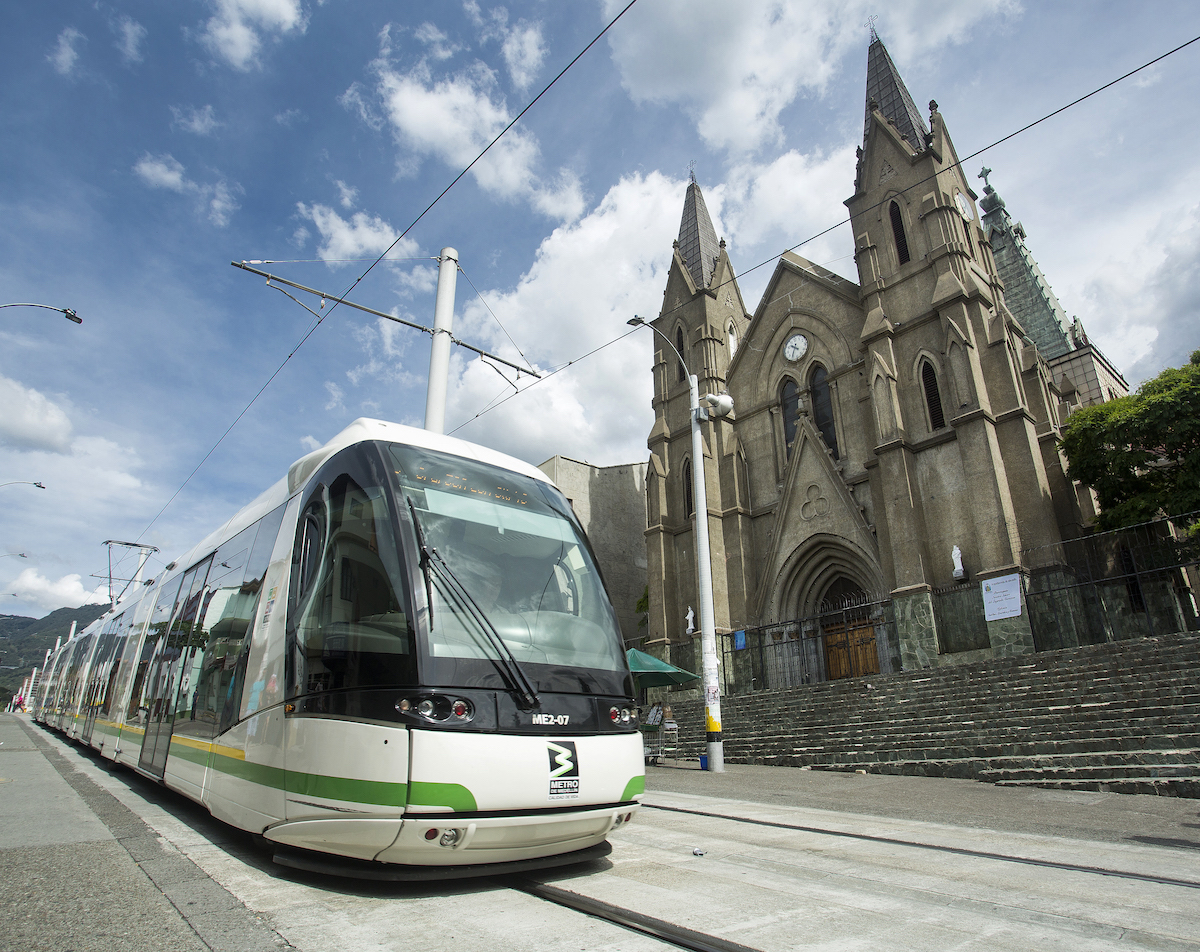 A tram passes a small church in Medellin, Colombia