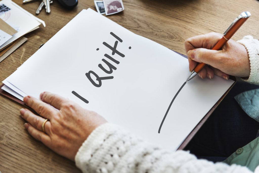 "I quit" is written on paper to represent a resignation letter as someone hands in their notice