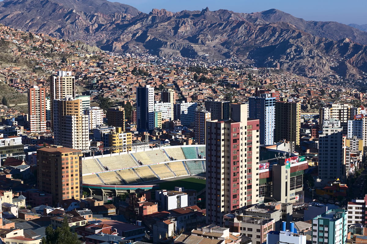 A football stadium in a busy city centre with mountains in the background.