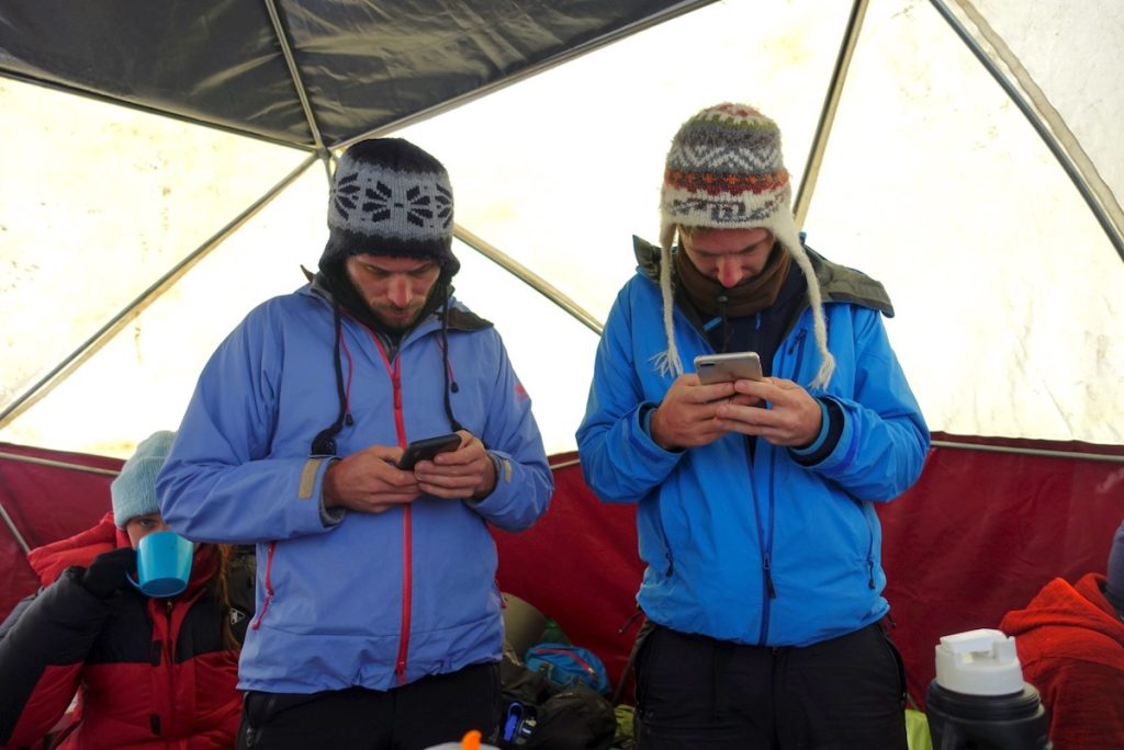 Two men in cold weather clothing check their phones intensely 