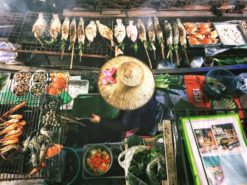 A food vendor in a traditional Thai hate serves seafood at a street stall