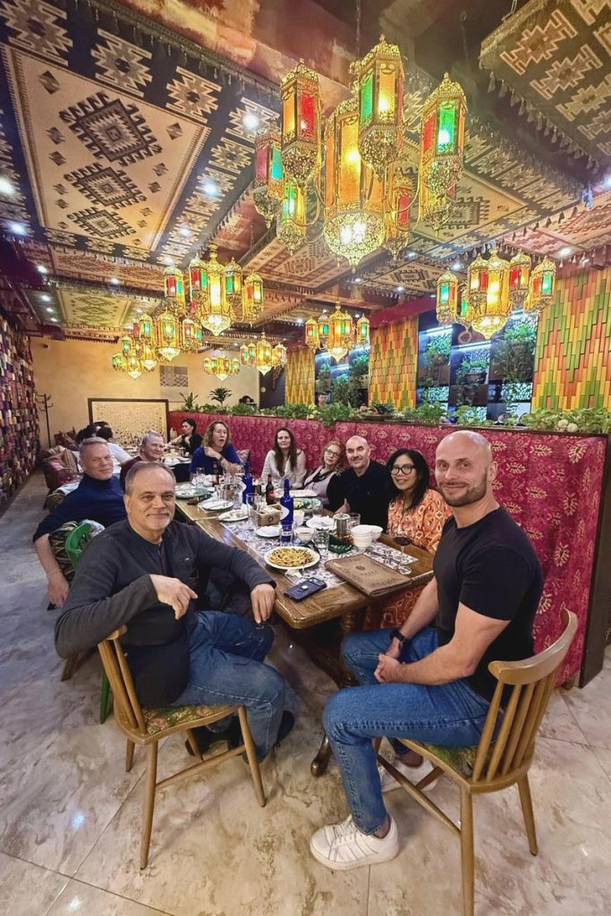 Tour group at a long table under coloured lanterns in a traditional restaurant in Almaty