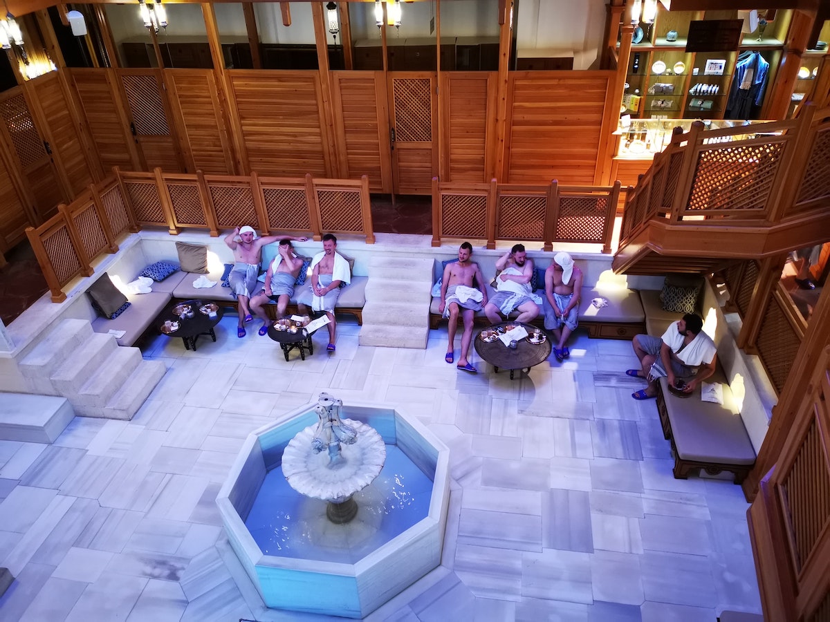 Men sit and talk with each other with towels around their waists in a Turkish hammam.