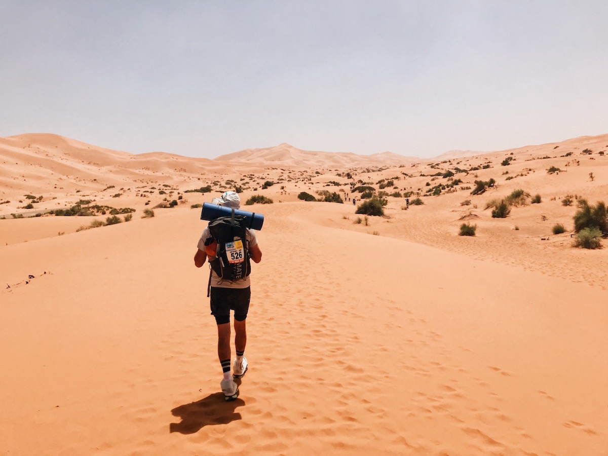 A male ultramarathon runner walks alone through the Sahara Desert during The Marathin Des Sables race