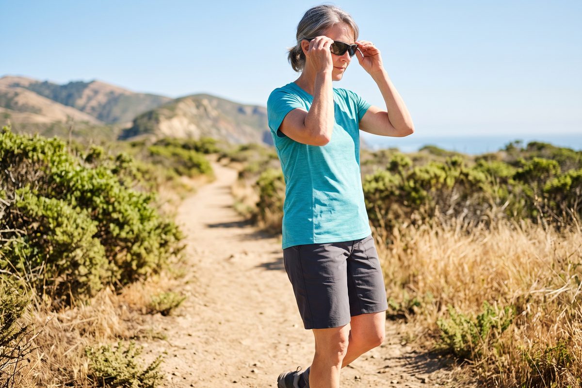 Best Sunglasses After Cataract Surgery: What to Look For | woman putting on sunglasses coastal trail Woman putting on sunglasses before a hike on a sunny coastal trail